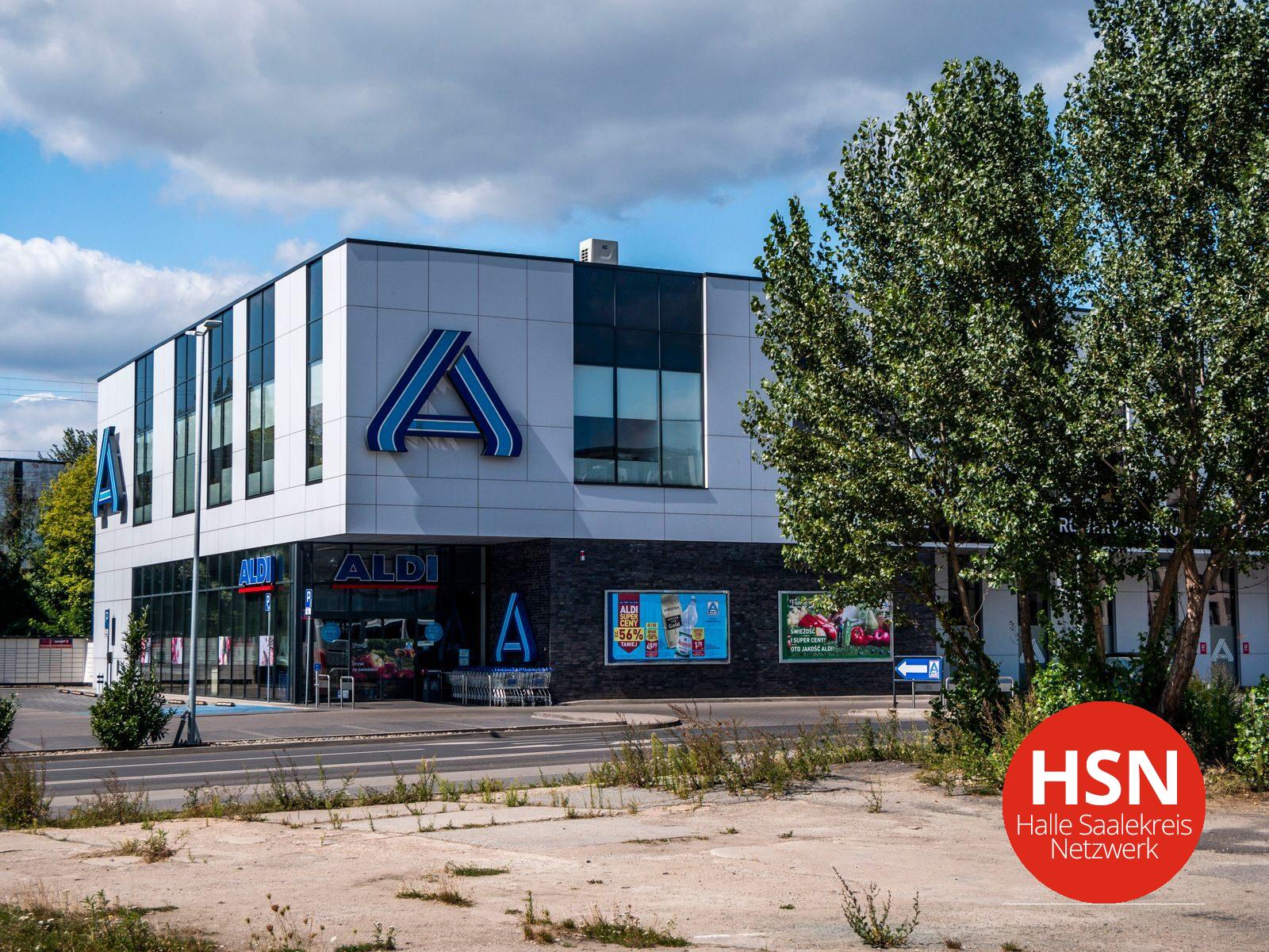 Blue and white modern Aldi store exterior surrounded by green trees under a clear sky